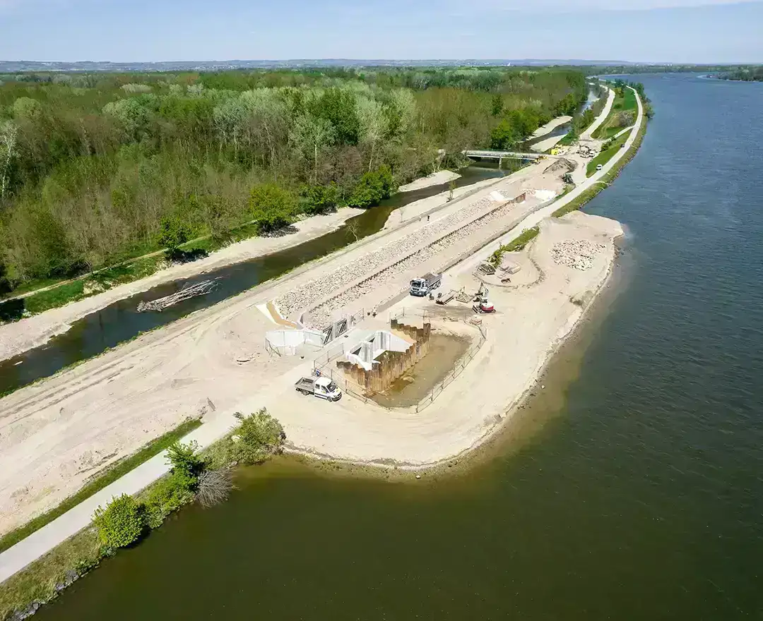 A view from above of the construction sites at the Altenwörth fish migration aid: excavators and heavy goods vehicles are at work. The sky is blue and the sun is shining.